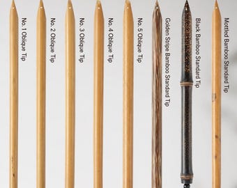 May include: A collection of eight bamboo dip pens for calligraphy, labeled Bamboo Dip Pen and Tibetan Calligraphy Pen. The set includes five light bamboo pens with oblique tips, one golden stripe bamboo pen, one black bamboo pen, and one mottled bamboo pen, each with a small black hanging loop.