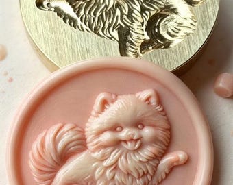 May include: A circular brass wax seal stamp featuring an engraved Pomeranian dog design, paired with a matching light pink wax seal impression that displays the same detailed dog figure with a fluffy coat and raised paw.