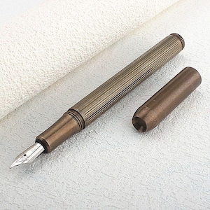 Puede incluir: Una pluma estilogr&aacute;fica de color bronce con un cuerpo acanalado y un plum&iacute;n plateado. El capuch&oacute;n est&aacute; separado y colocado junto a la pluma. El instrumento de escritura mide unos 14 cm de largo.