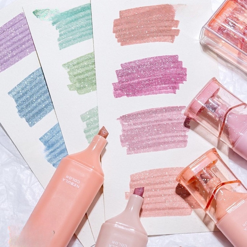 May include: A collection of pastel-colored highlighters with glittery ink, each with a different shade. The highlighters are peach-colored with the text "NEBULA COLOR" printed on them. Swatches of the ink are shown on white paper, including purple, blue, green, and pink.