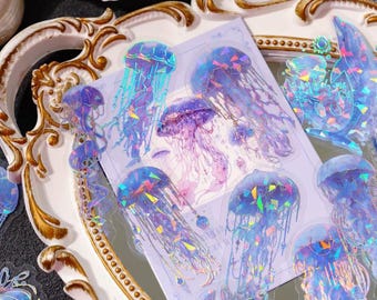 May include: A collection of translucent stickers featuring holographic jellyfish designs in shades of blue, purple, and pink. The stickers display intricate tentacle details and geometric light-reflecting patterns on a clear adhesive backing.