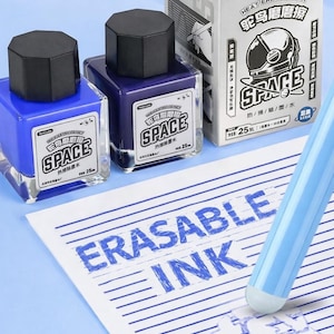 May include: Two square glass bottles of heat erasable ink with black octagonal caps, one blue and one purple, alongside their matching cardboard box labeled SPACE. A light blue pen is shown erasing the blue text ERASABLE INK on lined paper.