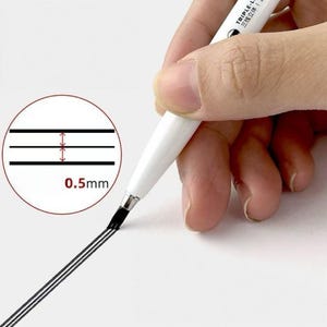 May include: A white pen with black ink is used to draw three parallel lines on white paper. A circular inset shows the lines are 0.5mm apart. The pen has the text "TRIPLE-LINE" on the side.