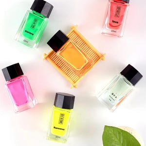 May include: An overhead shot of several small, rectangular perfume bottles with black caps. The bottles contain colorful liquids in shades of green, pink, yellow, orange, and red. Each bottle has text in a foreign language and the word "aurora", "lava", and "fluorescence".