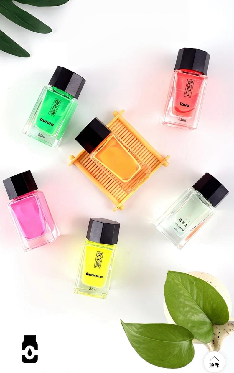May include: An overhead shot of several small, rectangular perfume bottles with black caps. The bottles contain colorful liquids in shades of green, pink, yellow, orange, and red. Each bottle has text in a foreign language and the word "aurora", "lava", and "fluorescence".