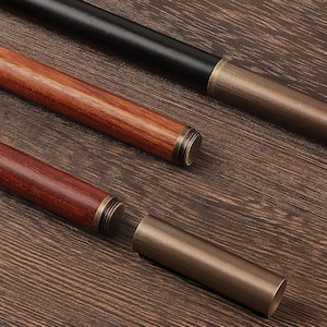 May include: Close-up of three pen holders. One is black, and two are wood-toned. Each pen holder has a metal end cap. One of the wood-toned pen holders is disassembled, showing the metal tube that holds the pen.