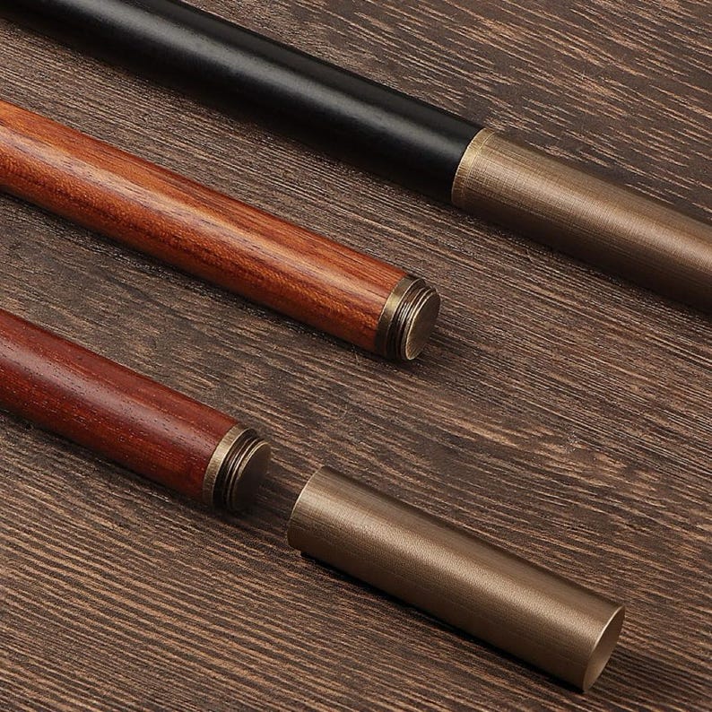 May include: Close-up of three pen holders. One is black, and two are wood-toned. Each pen holder has a metal end cap. One of the wood-toned pen holders is disassembled, showing the metal tube that holds the pen.