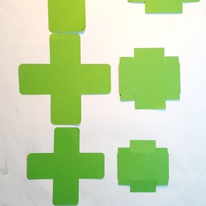 K&ouml;nnte beinhalten: F&uuml;nf gr&uuml;ne Papier-Schablonen zum Basteln von Boxen. Die Schablonen haben die Form eines Pluszeichens mit Laschen an den Seiten. Die Schablonen sind nach Gr&ouml;&szlig;e geordnet, die gr&ouml;&szlig;te oben und die kleinste unten.