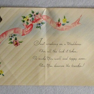 May include: A vintage greeting card with a cream-colored background featuring diagonal stripes. The card is decorated with a pink ribbon and small floral clusters in pink, yellow, and blue. The text reads: Just wishing on a Wishbone, For all the luck it takes, To make You well and happy soon, For You deserve the breaks!