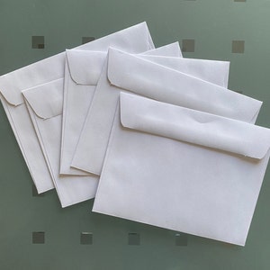 Puede incluir: Cinco sobres blancos apilados uno encima del otro. Los sobres son todos del mismo tama&ntilde;o y forma.