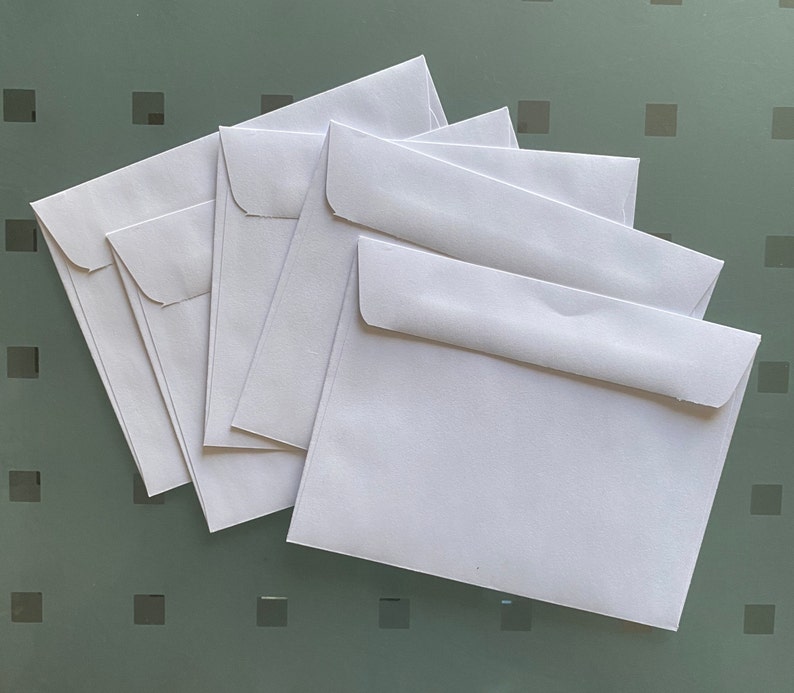 Puede incluir: Cinco sobres blancos apilados uno encima del otro. Los sobres son todos del mismo tama&ntilde;o y forma.