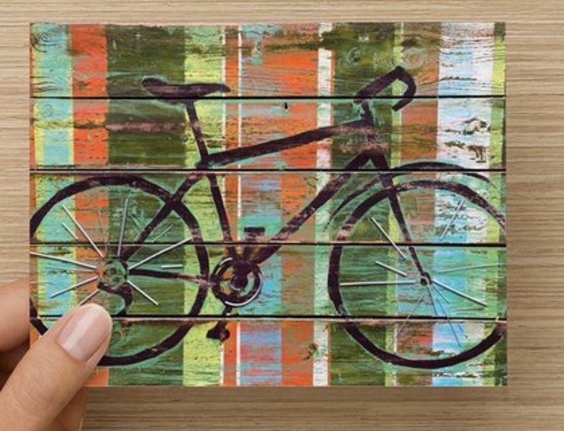 Puede incluir: Una silueta de bicicleta negra sobre un fondo de rayas de colores. El fondo est&aacute; hecho de tablones de madera pintados en tonos de azul, verde, naranja y rojo.