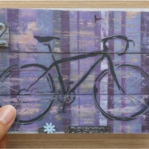 Puede incluir: Una silueta negra de una bicicleta con un fondo a rayas p&uacute;rpuras y blancas. El n&uacute;mero "2" es visible en la esquina superior izquierda.