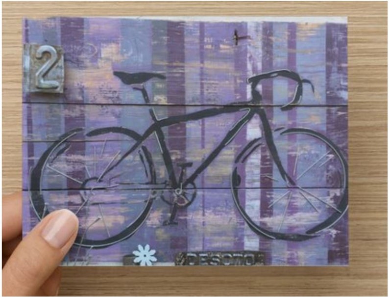 Puede incluir: Una silueta negra de una bicicleta con un fondo a rayas p&uacute;rpuras y blancas. El n&uacute;mero "2" es visible en la esquina superior izquierda.