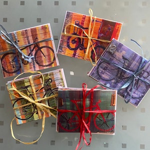 Puede incluir: Cinco tarjetas coloridas con ilustraciones de bicicletas. Cada tarjeta tiene un esquema de color y un dise&ntilde;o diferente. Las tarjetas est&aacute;n atadas con una cuerda.