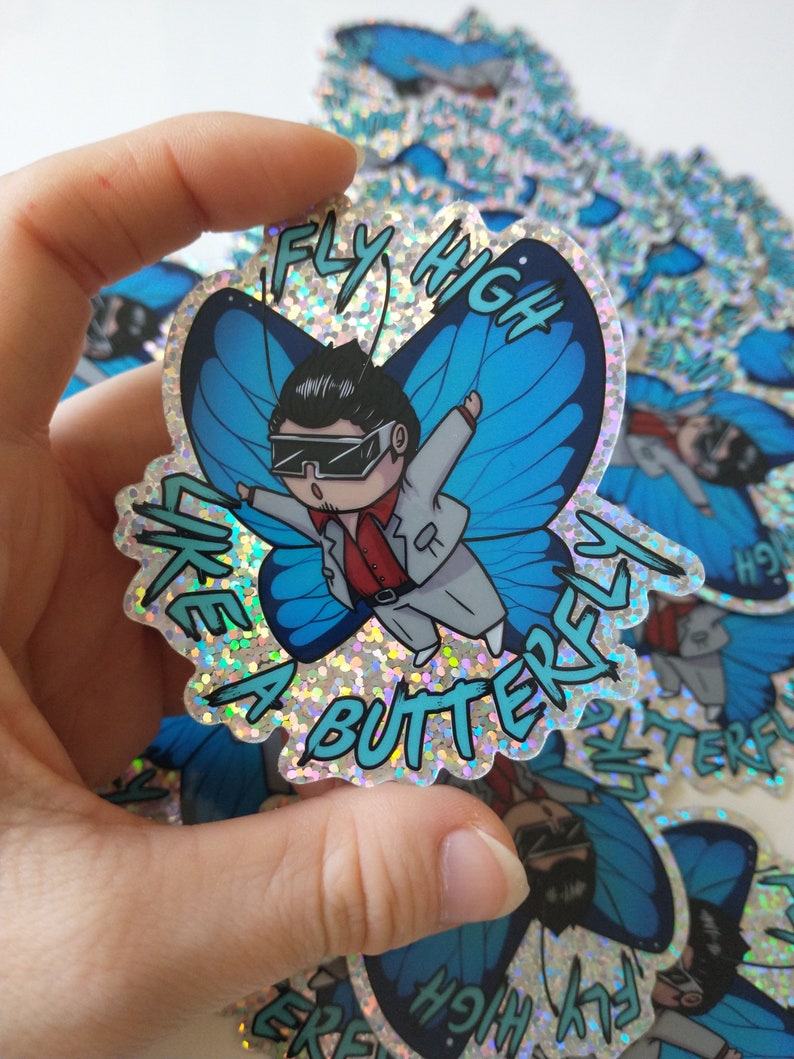 May include: A glittery sticker with a cartoon character dressed in a white suit and sunglasses, flying like a butterfly with blue wings. The sticker says "Fly High Like A Butterfly".