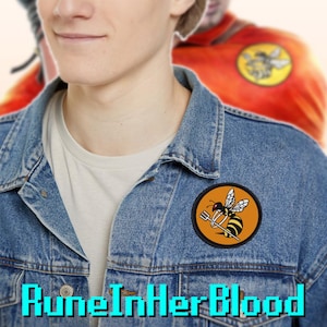 May include: A denim jacket with a round patch featuring a cartoon bee holding a fork. The patch is on a denim jacket. The text "RuneInHerBlood" is at the bottom of the image.