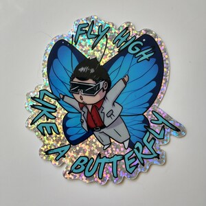 May include: A holographic sticker with a blue butterfly and a cartoon character flying with the text "Fly High Like A Butterfly".