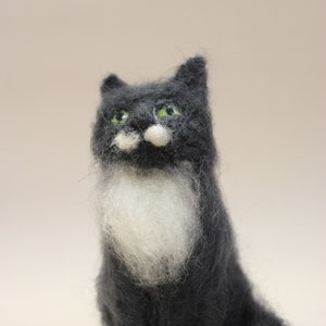 May include: A hand-felted black and white cat with green eyes. The cat is sitting with its paws tucked underneath it and its tail curled behind it.