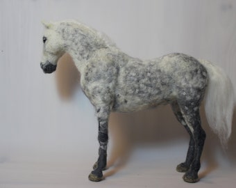 May include: A hand-felted gray and white horse with a long white tail and black hooves. The horse is standing on a white surface.