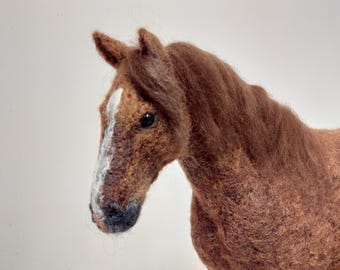 May include: A handcrafted felt horse sculpture. The horse has a brown body with a white stripe down its face. The mane and tail are a darker shade of brown. The horse is a detailed, three-dimensional art piece.
