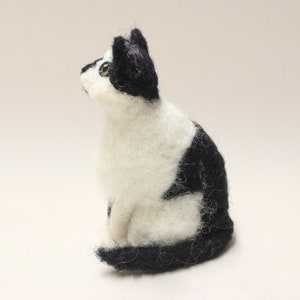 May include: A black and white felted cat figurine. The cat is sitting with its head turned to the side and its tail curled around its body.