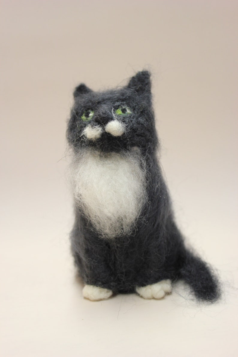 May include: A hand-felted black and white cat with green eyes. The cat is sitting with its paws tucked underneath it and its tail curled behind it.