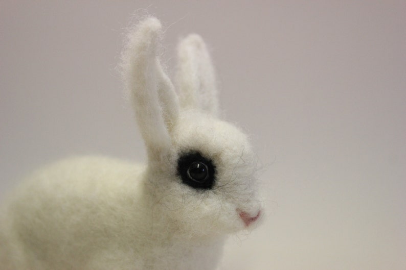 May include: A white fluffy rabbit with black eyes. The rabbit is made of felt and has a soft, cuddly appearance.