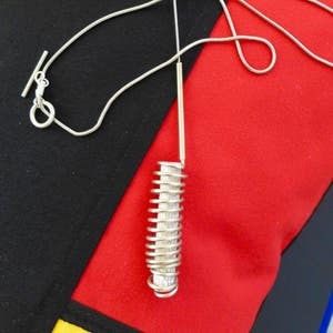 May include: A silver necklace with a coiled spring pendant. The necklace is on a black and red background.