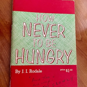 May include: A red and green book titled "How Never To Be Hungry" by J.I. Rodale. The book cover has a price of $1.00 and handwritten text that says "Read this and weef- EAT SLOWLY".