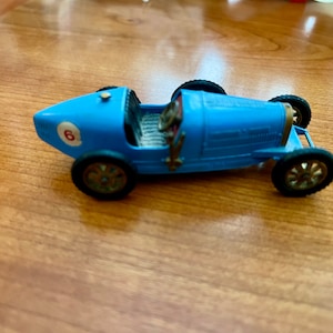 May include: A blue toy car with a number 6 on the side. The car has a driver in the seat and four wheels.
