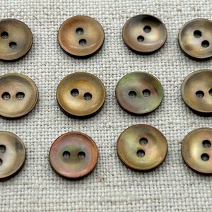 May include: A collection of 12 iridescent brown two-hole buttons. The buttons are round and have a smooth, slightly domed surface.