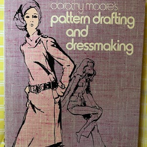 May include: A hardcover book titled Dorothy Moore's Pattern Drafting and Dressmaking. The cover features a purple and white grid background with black ink illustrations of two figures wearing dresses and the book title in bold white lettering.