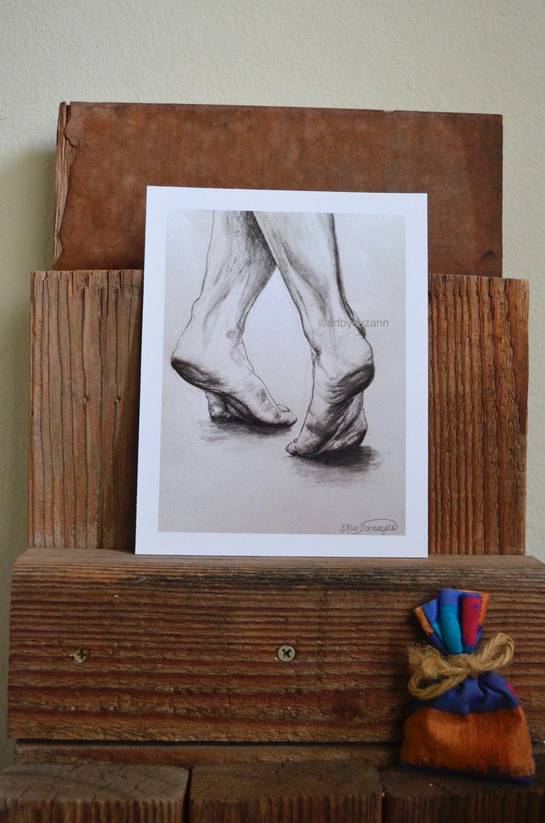 May include: A black and white pencil drawing of two bare feet, one foot is stepping forward, the other foot is behind it. The drawing is on a white background and is framed in a white mat.