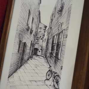 May include: Black and white pen and ink drawing of a narrow alleyway with a bicycle parked at the end. The alleyway is lined with buildings on both sides, and the drawing is framed in a wooden frame.