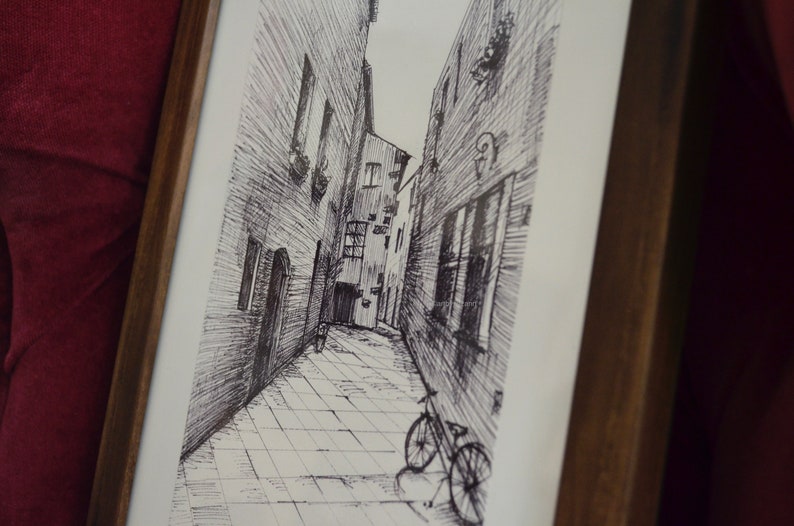 May include: Black and white pen and ink drawing of a narrow alleyway with a bicycle parked at the end. The alleyway is lined with buildings on both sides, and the drawing is framed in a wooden frame.