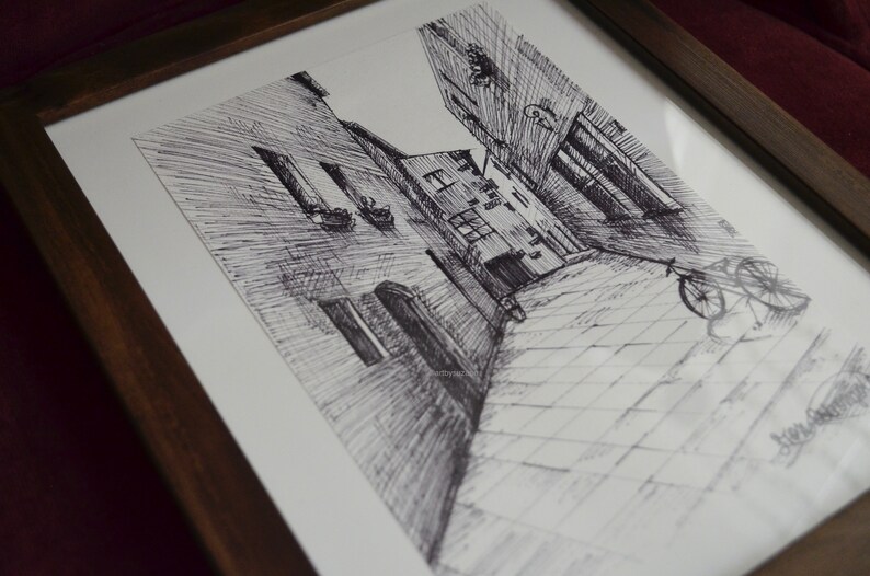 May include: A black and white ink drawing of a narrow street in a European city. The street is lined with tall buildings and there is a bicycle parked on the cobblestone street.