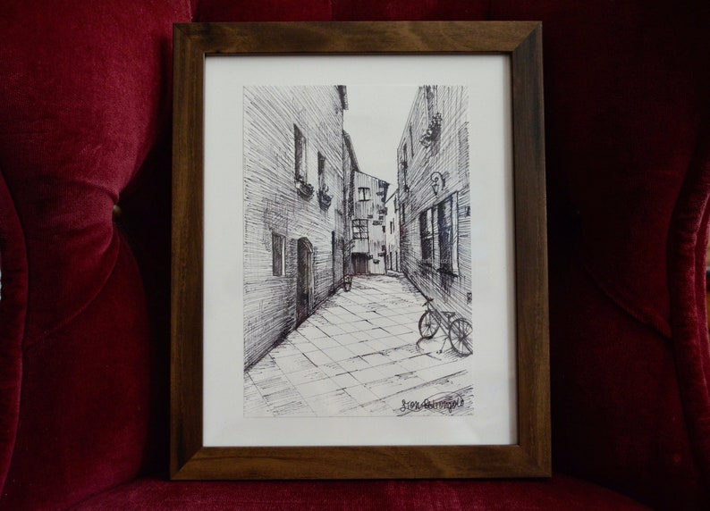 May include: A black and white ink drawing of a narrow street in a European city. The street is lined with tall buildings and there is a bicycle parked in the middle of the street.