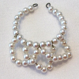May include: A vintage pearl necklace with a unique design. The necklace features multiple strands of faux pearls, connected to form a distinctive shape. The pearls are a creamy white color, and the necklace has a delicate, feminine aesthetic.