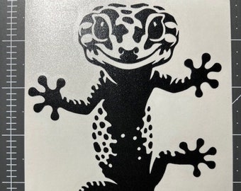 Può includere: Silhouette di geco in bianco e nero con un viso sorridente e un motivo a macchie. Il geco è arrotolato con la coda avvolta attorno al suo corpo.