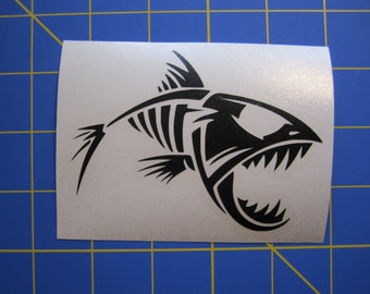 Può includere: Adesivo in vinile bianco e nero di uno scheletro di pesce con la bocca aperta e denti affilati. Il pesce è rivolto a destra e ha un design stilizzato.
