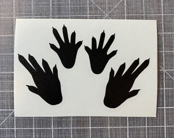 Può includere: Quattro impronte di mani nere in silhouette su uno sfondo bianco. Le impronte di mani hanno una forma a artiglio con quattro dita e un pollice.