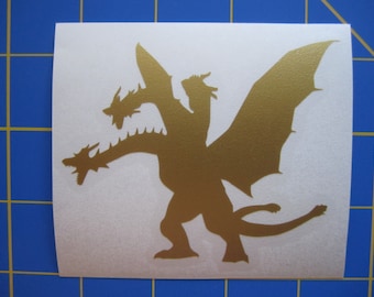 Può includere: Adesivo in vinile color oro raffigurante un drago a tre teste con grandi ali e una lunga coda. Il drago è mostrato in una posa dinamica. L'adesivo è su sfondo bianco. Il drago è una creatura mitica.