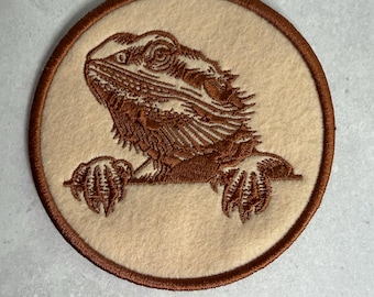 Può includere: Toppa rotonda ricamata con un drago barbuto marrone. Il drago è posto su uno sfondo color crema, con un bordo marrone. Il ricamo dettagliato evidenzia le caratteristiche del drago. Adatta agli amanti dei rettili, circa 10 cm di diametro.