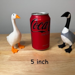 May include: Two decorative goose figurines, one white with orange beak and feet, the other gray, black, and white. A red Coca-Cola Zero can is between them. The text "5 inch" (approx. 13 cm) is at the bottom.