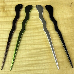 May include: Four hair sticks made of metal with a wavy design. The sticks are in black, green, silver, and dark brown.
