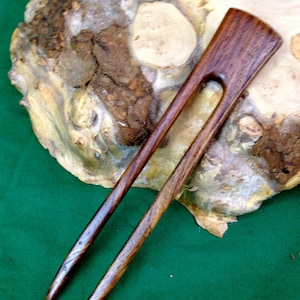 May include: A pair of dark brown wooden hair sticks with a smooth, polished finish. The sticks are tapered at the ends and have a small hole in the center of the top stick.