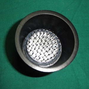 May include: A black plastic cup with a circular metal base with many small metal pins. The pins are arranged in a circular pattern and are evenly spaced.