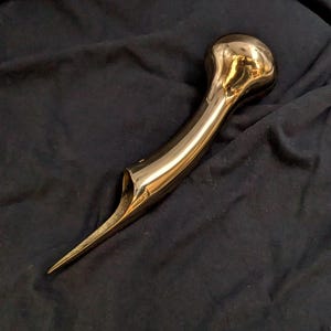 Puede incluir: Un mango de bast&oacute;n de metal de color dorado con una parte superior redondeada y bulbosa y una punta larga y puntiaguda.