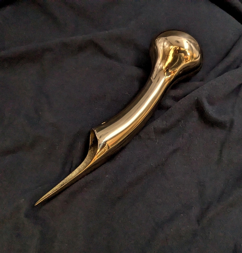 Puede incluir: Un mango de bast&oacute;n de metal de color dorado con una parte superior redondeada y bulbosa y una punta larga y puntiaguda.